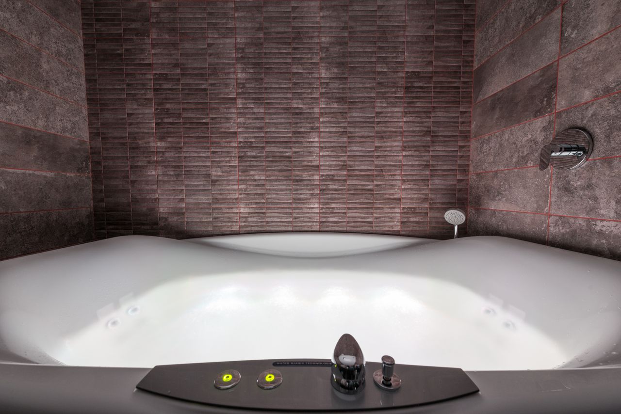 Modern white ceramic tub with illumination and contemporary control panel with buttons and levers placed in stylish bathroom among walls